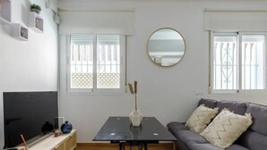 Una sala de estar con televisor, una mesa con un jarrón y un sofá con almohadones.