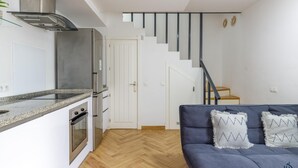 Une cuisine moderne dotée d’un four encastré et d’appareils électroménagers en acier inoxydable, d’un parquet en bois disposé en motif à chevrons et d’un escalier menant à un balcon.