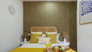 Une chambre d’hôtel avec un lit, des tables de chevet, un plateau avec le petit-déjeuner et un mur recouvert de lattes de bois verticales.