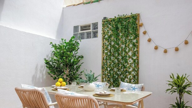 Un coin repas avec une table dressée pour quatre personnes, entourée de chaises en osier, d’une plante en pot et d’un mur végétal.
