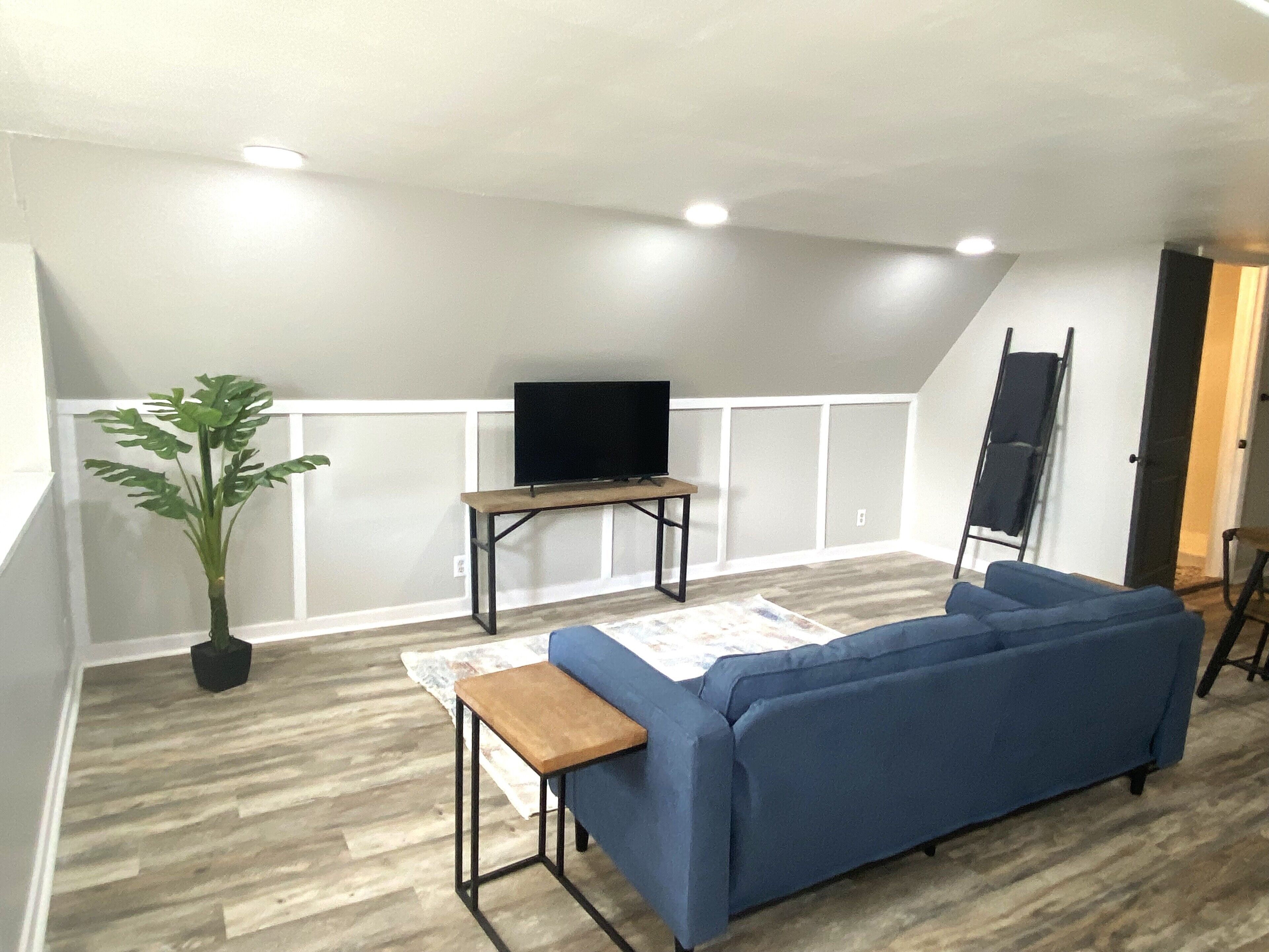 Une pièce avec un canapé bleu, une petite table en bois, une plante en pot et un téléviseur posé sur un meuble.