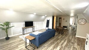 En moderne stue med en blå sofa, et træsofabord og et fjernsyn på et stativ.