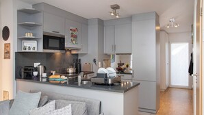 A modern kitchen with grey cabinets, a microwave, and a coffee maker. There is a grey sofa with patterned cushions in the living area. - Tasman S12/R by Interhome (Le Bouveret)