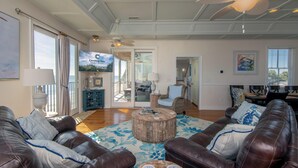 A spacious living room with leather sofas, a round coffee table, and a large window with curtains. - Moon Tide|Oceanfront Showplace|Dog Friendly|Elevator|Rooftop Deck|Family-Friendly Amenities (Edisto Beach)