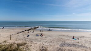 A beach with a stone wall, people relaxing, and a clear sky. - Moon Tide|Oceanfront Showplace|Dog Friendly|Elevator|Rooftop Deck|Family-Friendly Amenities (Edisto Beach)