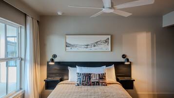 A bedroom with a bed, two bedside tables, a ceiling fan, a window with curtains, and a framed picture on the wall.