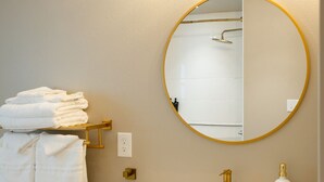 A bathroom with a white sink, gold fixtures, a round mirror with a gold frame, and a towel rack with folded towels. - Gloria Inn 2 -5 minutes from Baylor and 2 Blocks to Magnolia (Waco)