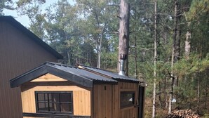 Una cabaña de madera pequeña con un porche, una silla y un balde.