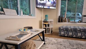 Una sala de estar con televisión en la pared, una mesa de centro, una estantería y un sofá estampado.