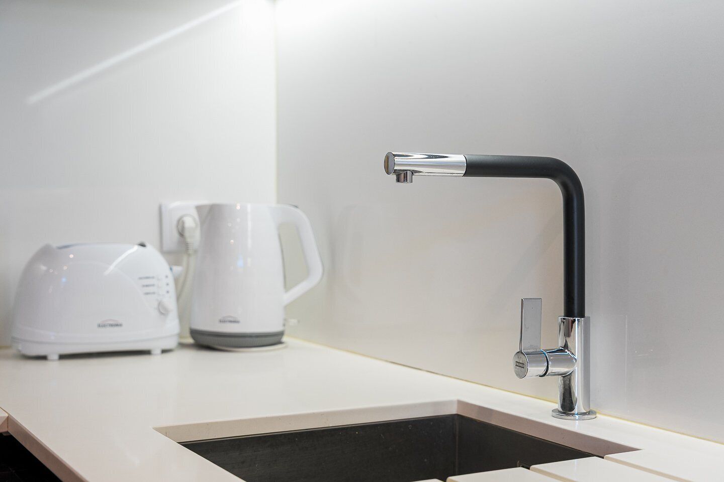 A modern kitchen with a black faucet, a white kettle, and a white coffee maker on the counter.