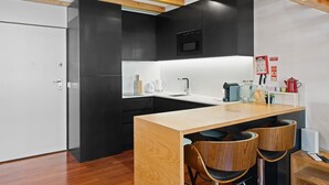 Une cuisine moderne avec des meubles de couleur noire, un plan de travail en bois et deux tabourets de bar.
