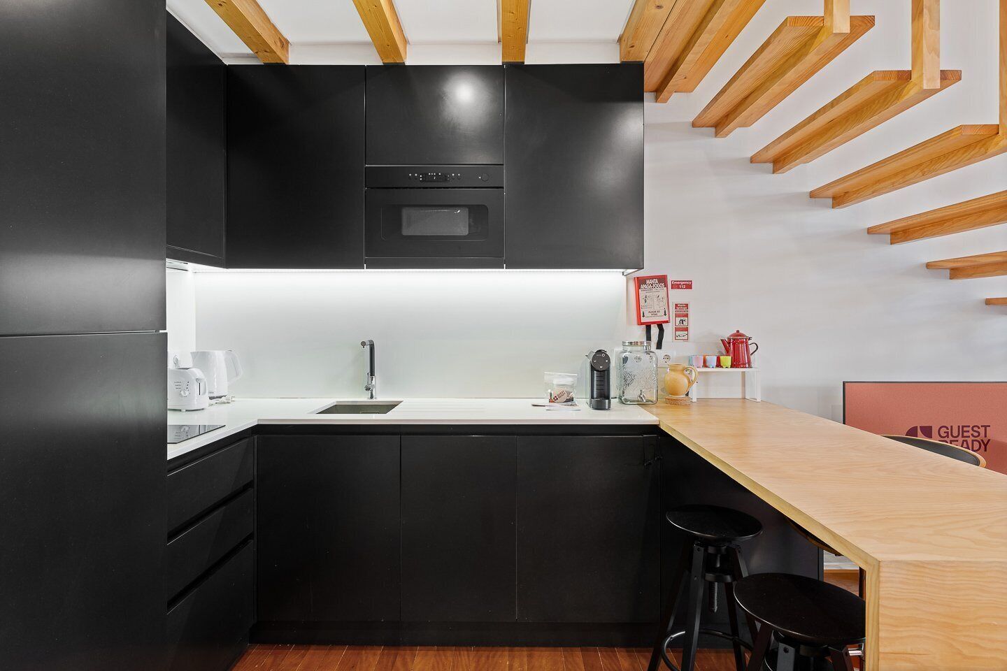 A modern kitchen with black cabinets, a wooden dining table, and a bar stool.