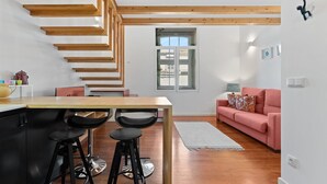 Une cuisine moderne avec un escalier en bois, un coin repas avec deux chaises noires et un canapé rose dans un salon lumineux.