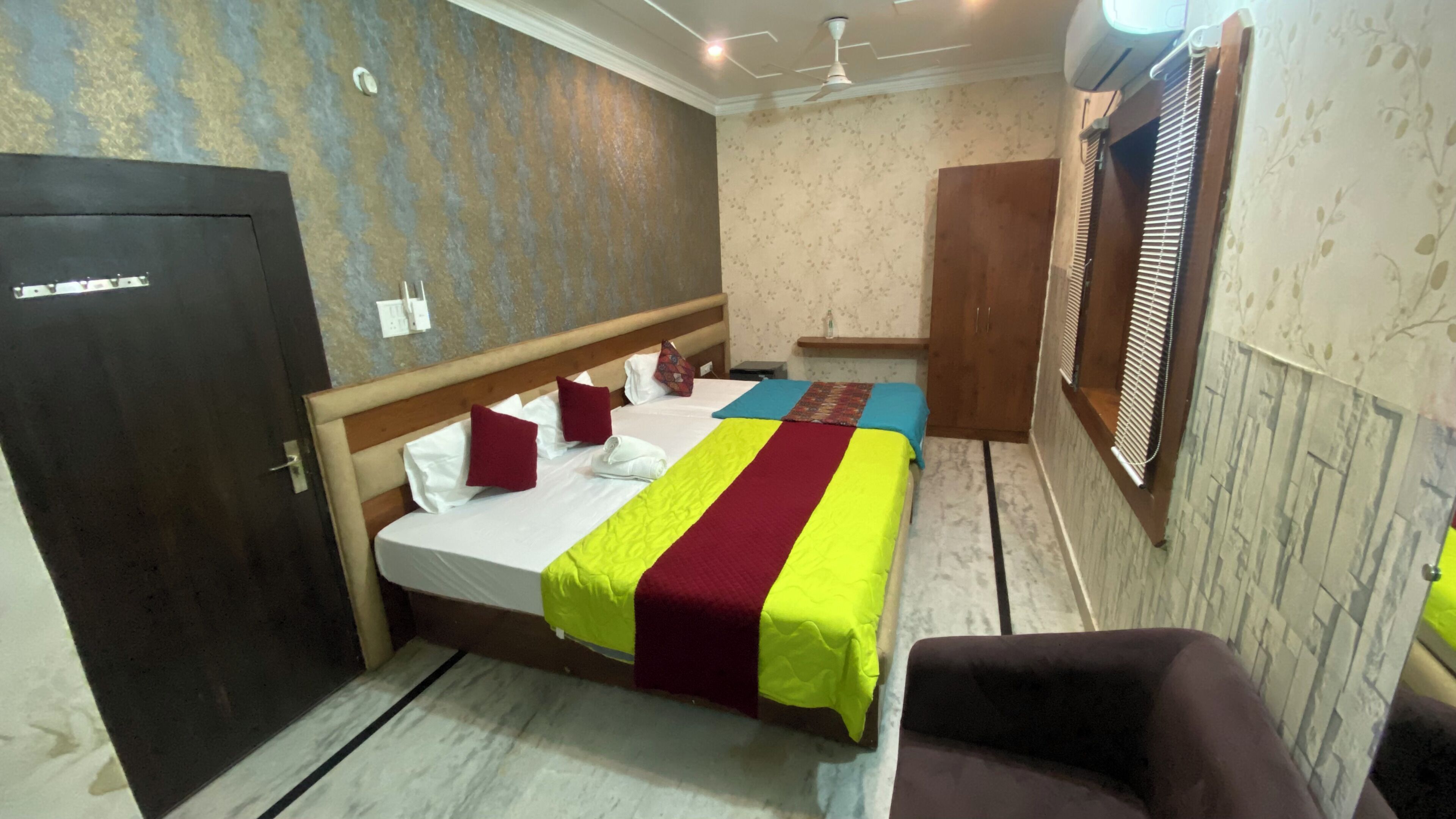 A hotel room with a bed, a chair, a wardrobe, and a window with blinds.