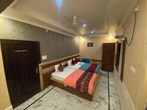 Habitación de hotel con dos camas, un armario, ventilador de techo, equipo de aire acondicionado y una pequeña mesa con una silla.