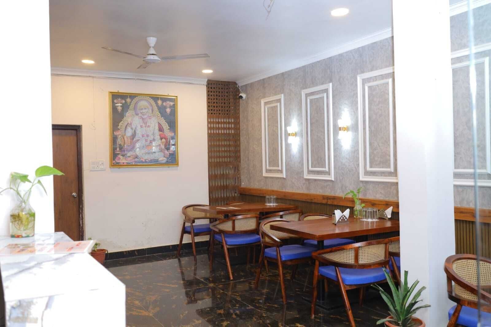 A restaurant with wooden tables and blue cushioned chairs, a ceiling fan, and a decorative painting on the wall.