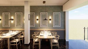 A dining area with tables set for four, wooden chairs, pendant lighting, and framed wall decorations.