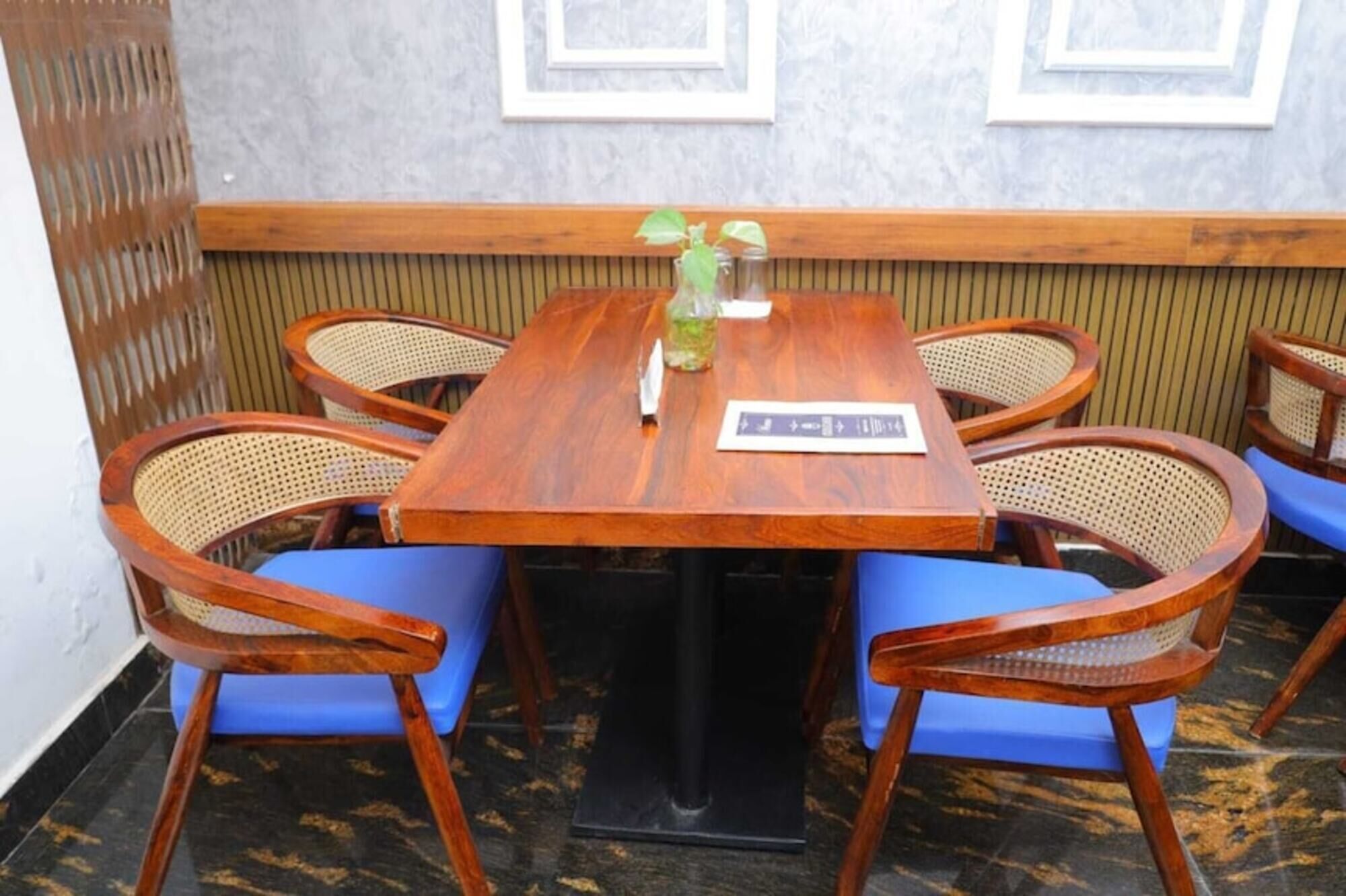 Een houten tafel met een bordje, omringd door rieten stoelen met blauwe kussens.