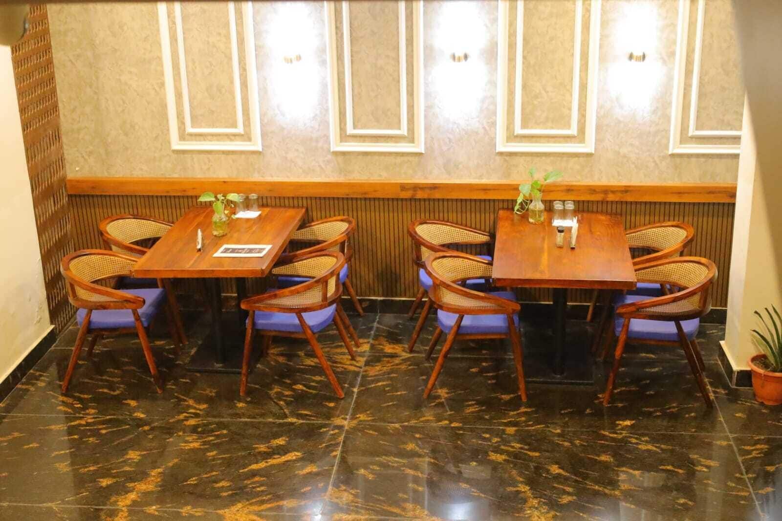 Un comedor con dos mesas de madera y sillas de mimbre, suelo de mármol y pared de madera con iluminación empotrada.