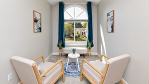 A room with two armchairs, a round table, and a view through a large arched window. - Modern Comfort in Des Moines` West Side 4BR/2.5BR (Clive)