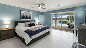Une chambre avec un lit, des tables de chevet, un ventilateur de plafond et une vue sur une piscine et un espace patio.