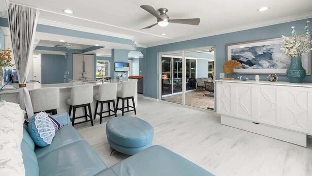 Un salon moderne avec un canapé bleu, un ventilateur de plafond et un coin cuisine à l’arrière-plan.