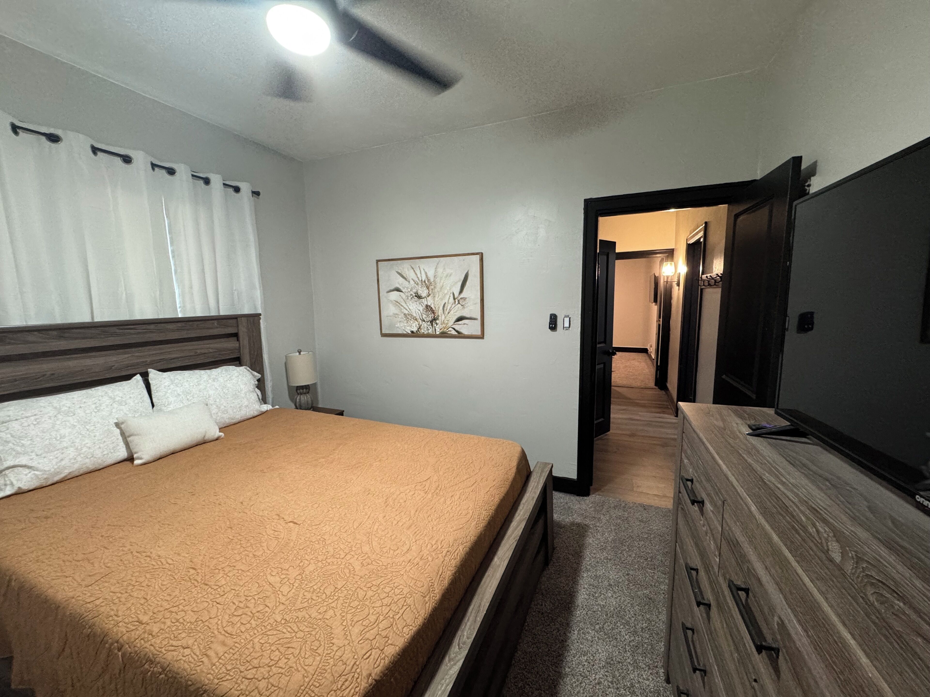 A bedroom with a bed, a dresser, a ceiling fan, a nightstand, a lamp, and a framed picture on the wall.