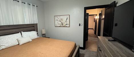 A bedroom with a bed, a dresser, a ceiling fan, a nightstand, a lamp, and a framed picture on the wall.
