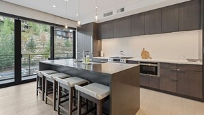 A modern kitchen with a large island, bar stools, and a view of the outdoors.