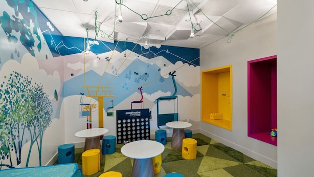 Zona infantil con paredes coloridas, mesas de juegos y unidades de almacenamiento.