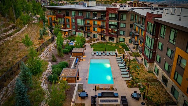 A modern hotel with a central pool, outdoor seating, and a mountainous backdrop.