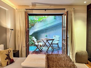 A room with a bed, a small table with chairs, a view of greenery outside, and a sliding door.