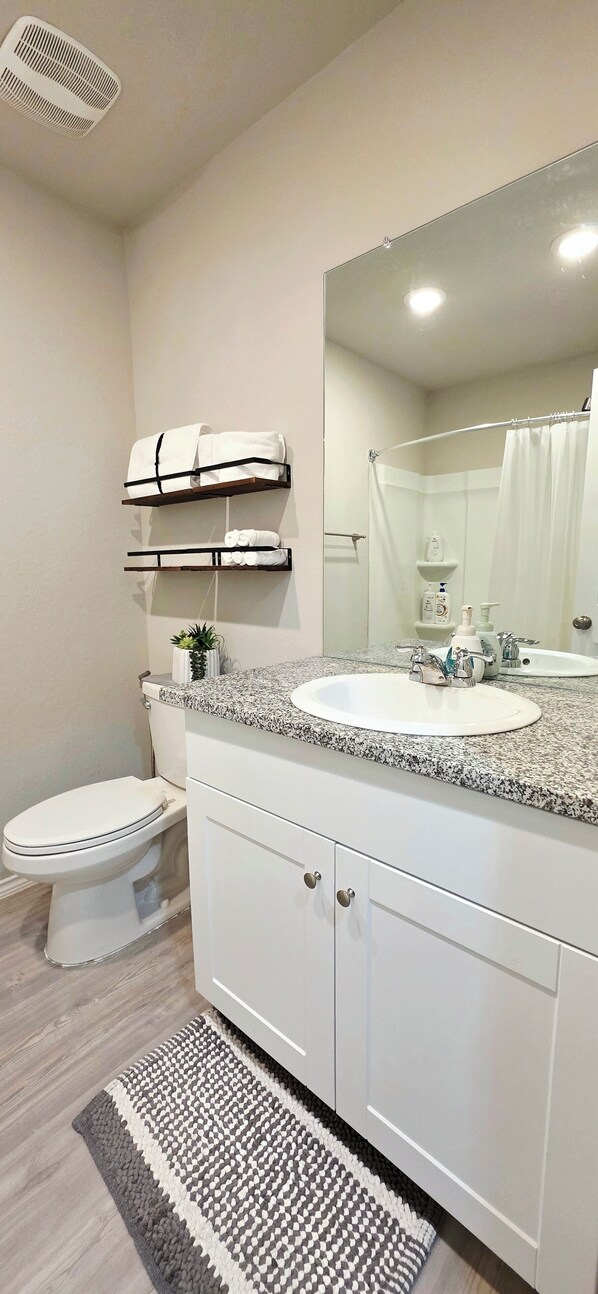 A bathroom with a white sink, a mirror, a towel rack, a toilet, and a shower curtain.