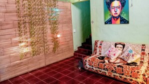 A room with a wooden wall covered in vines, a colorful sofa with floral patterns, and a painting of a person with a floral headpiece.