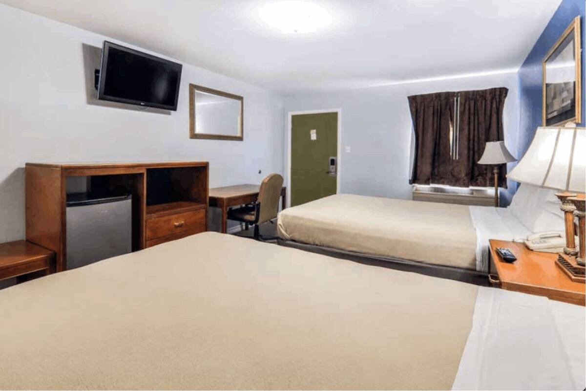 Une chambre d’hôtel avec deux lits, un bureau, une chaise, une télévision, un miroir et une fenêtre avec des rideaux.
