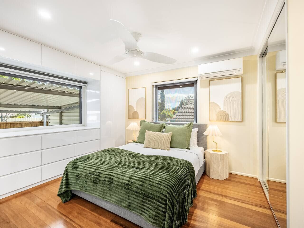 A modern bedroom with a large bed, a ceiling fan, and a window with a view of the outside.