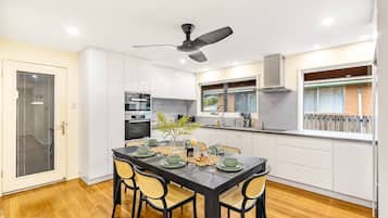 A modern kitchen with white cabinets, a dining table set for four, and a ceiling fan.