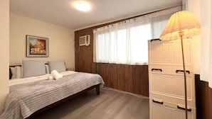Een slaapkamer met een bed, nachtkastje, lamp, kast en een raam met gordijnen.