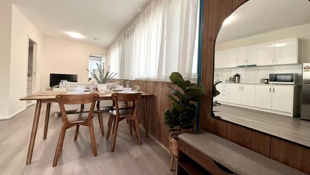 Een moderne eetruimte met een houten tafel en stoelen, een bankje, en een grote spiegel die de keuken weerspiegelt.