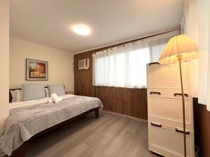 Une chambre à coucher avec un lit, une lampe de chevet, une fenêtre avec des rideaux et un climatiseur fixé au mur.