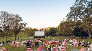 Een openluchttheater met een groot scherm, rijen grasstoelen en mensen die ernaar kijken.