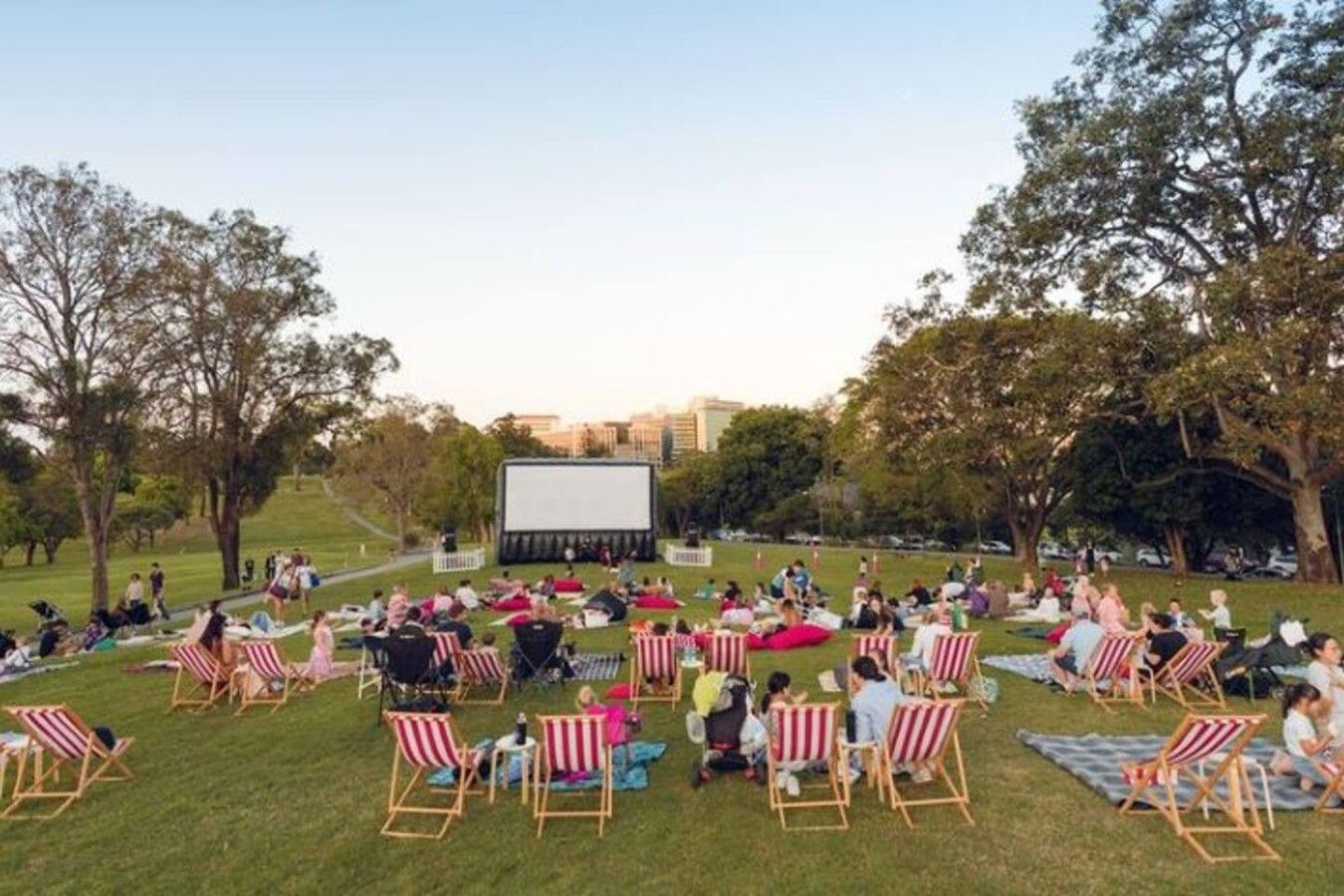 An outdoor movie screening area with a large screen, rows of striped chairs, and a grassy field.