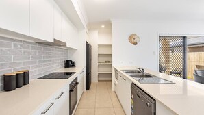 Een moderne keuken met witte kasten, een grijze betegelde spatwand en roestvrijstalen apparatuur.