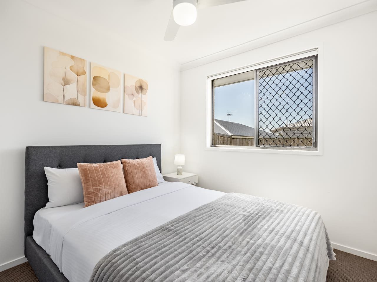 Un dormitorio con cama, mesita de noche, ventana con vistas y decoración en la pared.