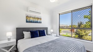 Een moderne slaapkamer met een groot bed, een nachtkastje, een wandairconditioner en een raam met uitzicht.