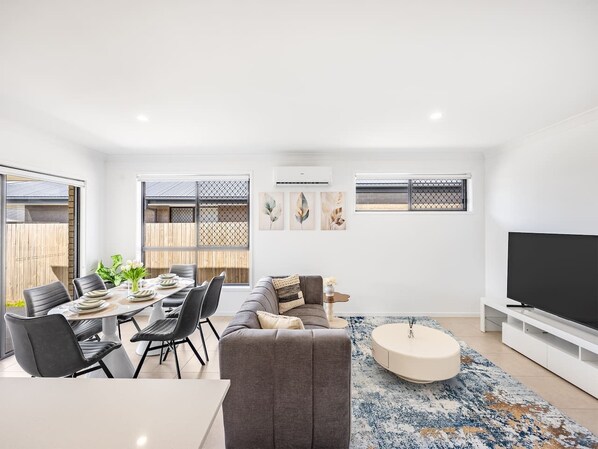 A modern living room with a dining area, a grey sofa, a round coffee table, and a flat-screen TV.