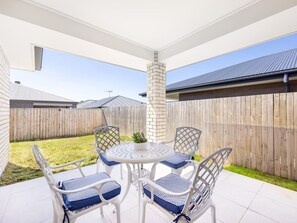 A patio with a round table and four chairs, surrounded by a wooden fence and a brick pillar.
