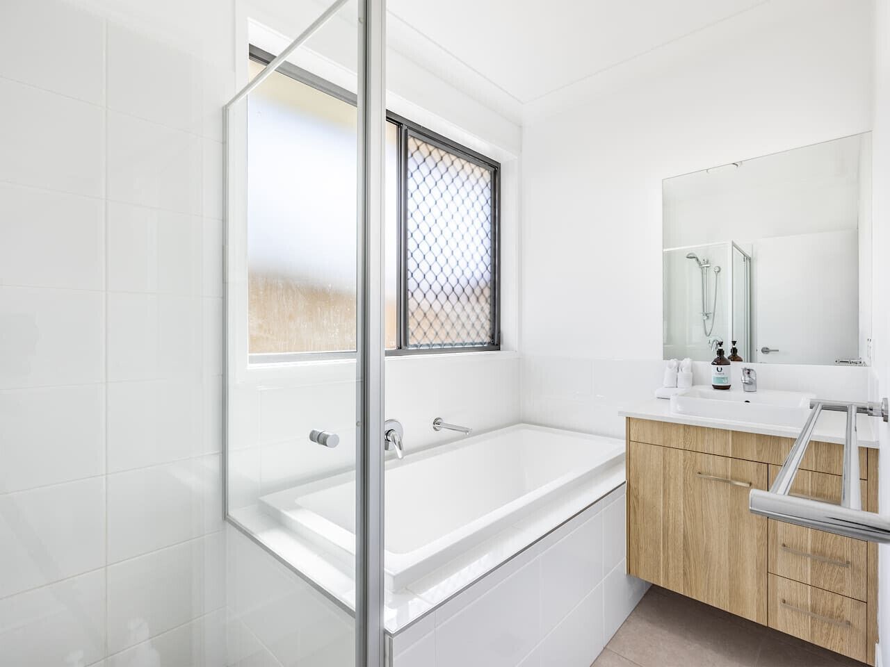 A modern bathroom with a glass-enclosed shower, a large bathtub, and a wooden vanity with a mirror.