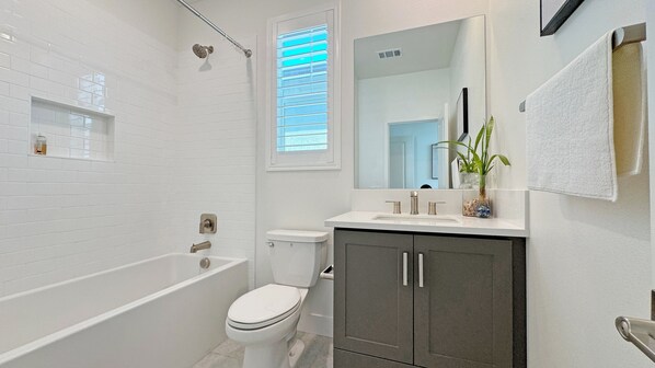 Un bagno moderno con una vasca da bagno bianca, un water e un lavandino con uno specchio sopra.