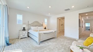 A bedroom with a large bed, a nightstand, a lamp, a chair with a yellow cushion, and a potted plant. - Fabulous 4-bedroom house with AC in irvine Lake Forest (Lake Forest)